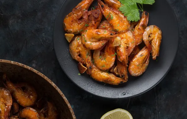 The dark background, table, lemon, plate, bowl, parsley, shrimp, fried