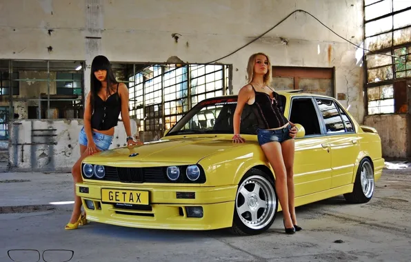 Girls, Two beautiful girls, look at the camera, standing near the old yellow car BMW, …