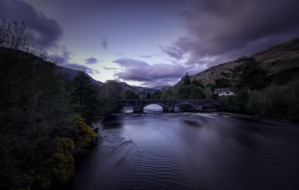The sky, clouds, trees, mountains, bridge, house, river, shore
