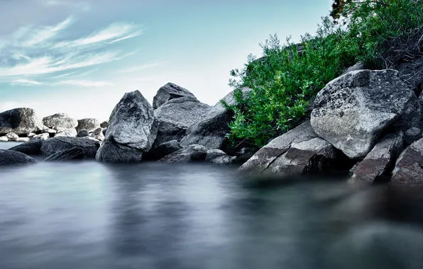 The sky, stones, shore, pond, boulders, shrubs