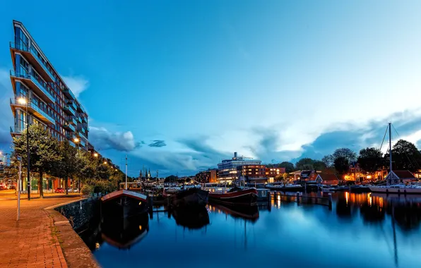 The sky, clouds, trees, lights, river, building, home, boats