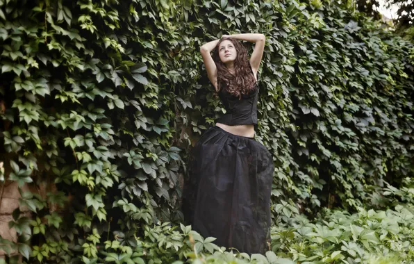 Girl, wall, plants, brunette, is, in black, posing