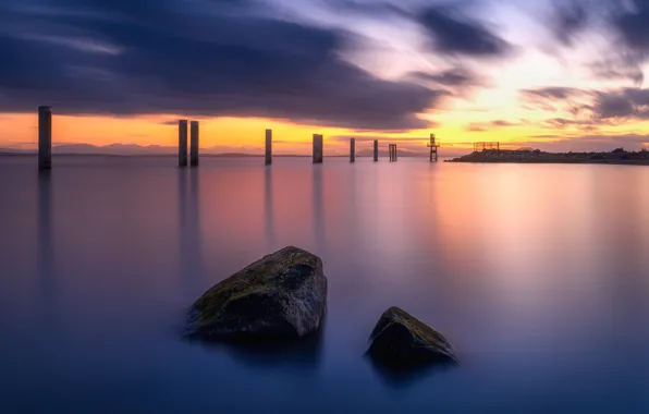 The sky, clouds, sunset, stones, shore, posts, pond, piles