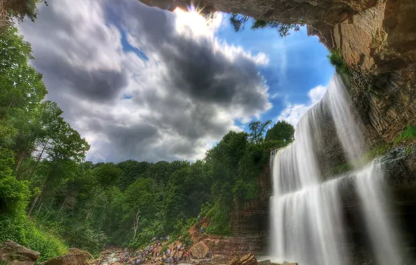 The sky, clouds, trees, rock, people, waterfall