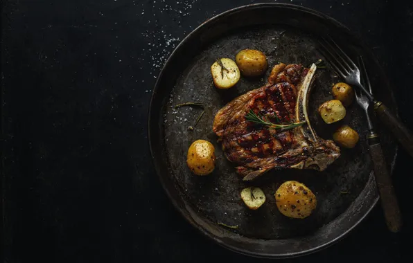 The dark background, meat, fork, spices, potatoes, pan, steak