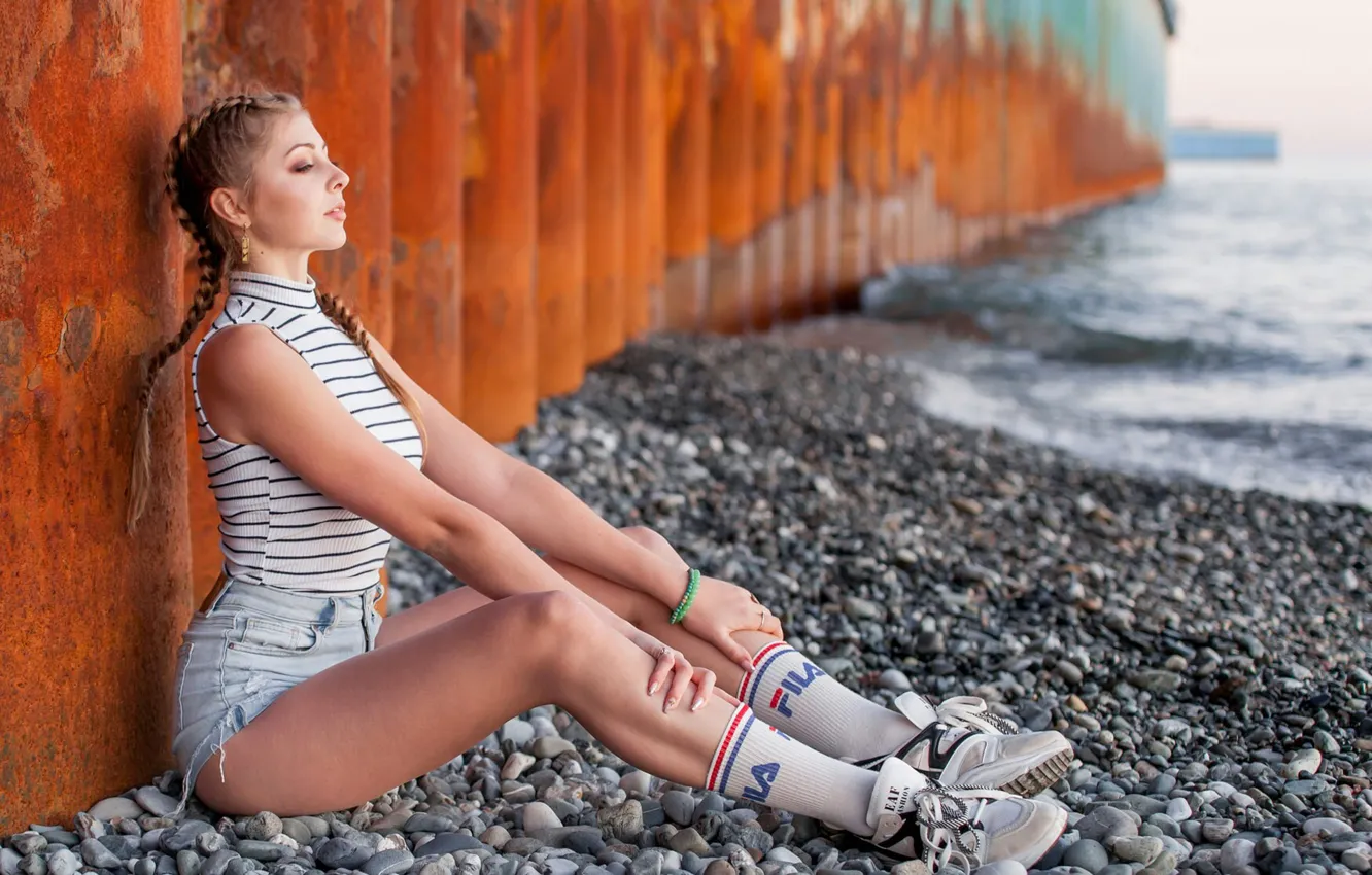 Photo wallpaper sea, stones, brunette, sitting, sneakers, jean shorts, Fila, looking away