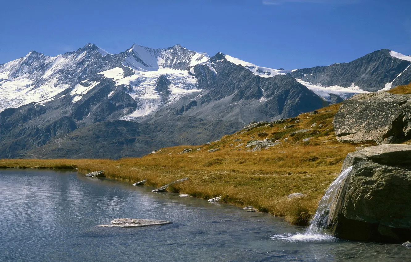 Photo wallpaper grass, mountains, lake, stones, shore, key, snowy